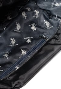 Černá textilní taška s námořnickou podšívkou a opakovaným bílým logem U.S. Polo Assn. Obsahuje zipové uzavření podél jedné hrany.