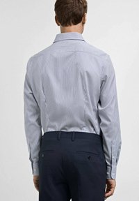 Takakatsview dari kemeja bergaris biru dan putih yang disesuaikan dengan lengan panjang, dipasangkan dengan celana gelap, menampilkan aksen kancing di manset dan saku.