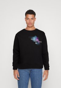 Sudadera negra de mezcla de algodón, con un diseño gráfico de texto colorido en el pecho, de corte holgado y cuello acanalado.