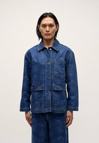 Denimjakke med blomstermønster, to frontlommer, knappestilling og en klassisk krage, vist mot en nøytral bakgrunn.