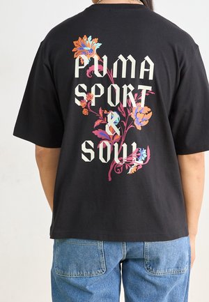 Czarna bawełniana koszulka z dużym kwiatowym wzorem i napisem "PUMA SPORT & SOUL" w pogrubionych białych literach na plecach.