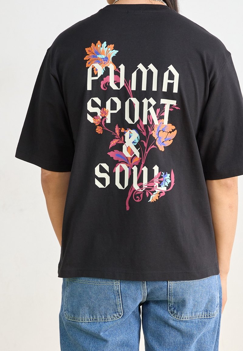 T-shirt en coton noir arborant un grand motif floral et le texte "PUMA SPORT & SOUL" en lettres blanches en gras au dos.