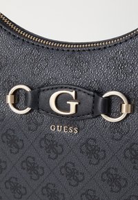 Zwarte handtas met textuur en gouden hardware, voorzien van een opvallend "G"-logo en ronde metalen accenten. Ritsdetail langs de bovenkant.