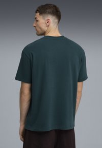 Camiseta de algodón de color verde oscuro con un corte relajado, mangas cortas y dobladillo recto, que presenta una textura suave sin marcas visibles.