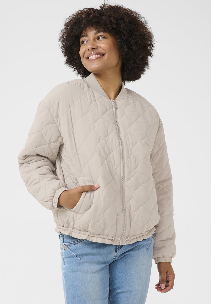 Veste bomber matelassée beige avec fermeture éclair devant, poignets côtelés, poches latérales et ourlet élastique. Texture lisse avec un motif en diamant.