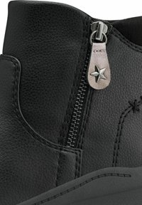 Botte de cheville en cuir noir avec une fermeture éclair sur le côté, dotée d'une tirette en forme d'étoile, d'une surface texturée et de détails de couture contrastés.