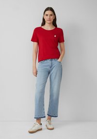 Rode katoenen t-shirt met een ronde hals en een kleine borduursel van fruit, gecombineerd met lichtblauwe wijde jeans en crèmekleurige sneakers.