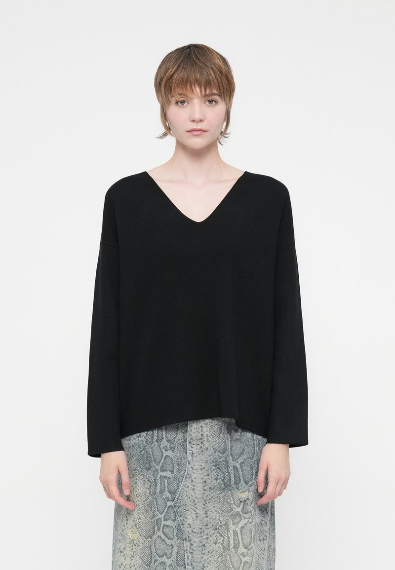 Black knitted sweater with a deep V-neck and long sleeves, paired with a light gray snake-print skirt. Smooth texture, relaxed fit.