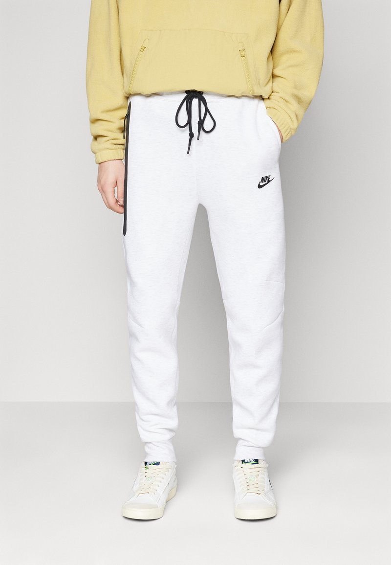 Pantalones de chándal blancos de Nike con detalles negros y cordón; combinados con una sudadera amarilla y zapatillas blancas. Diseño suave y casual.