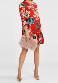 Červené květinové šaty s tříčtvrtečními rukávy a volánkovým lemem, v doplnění s huňatým růžovým psaníčkem a nahými vysokými podpatky.