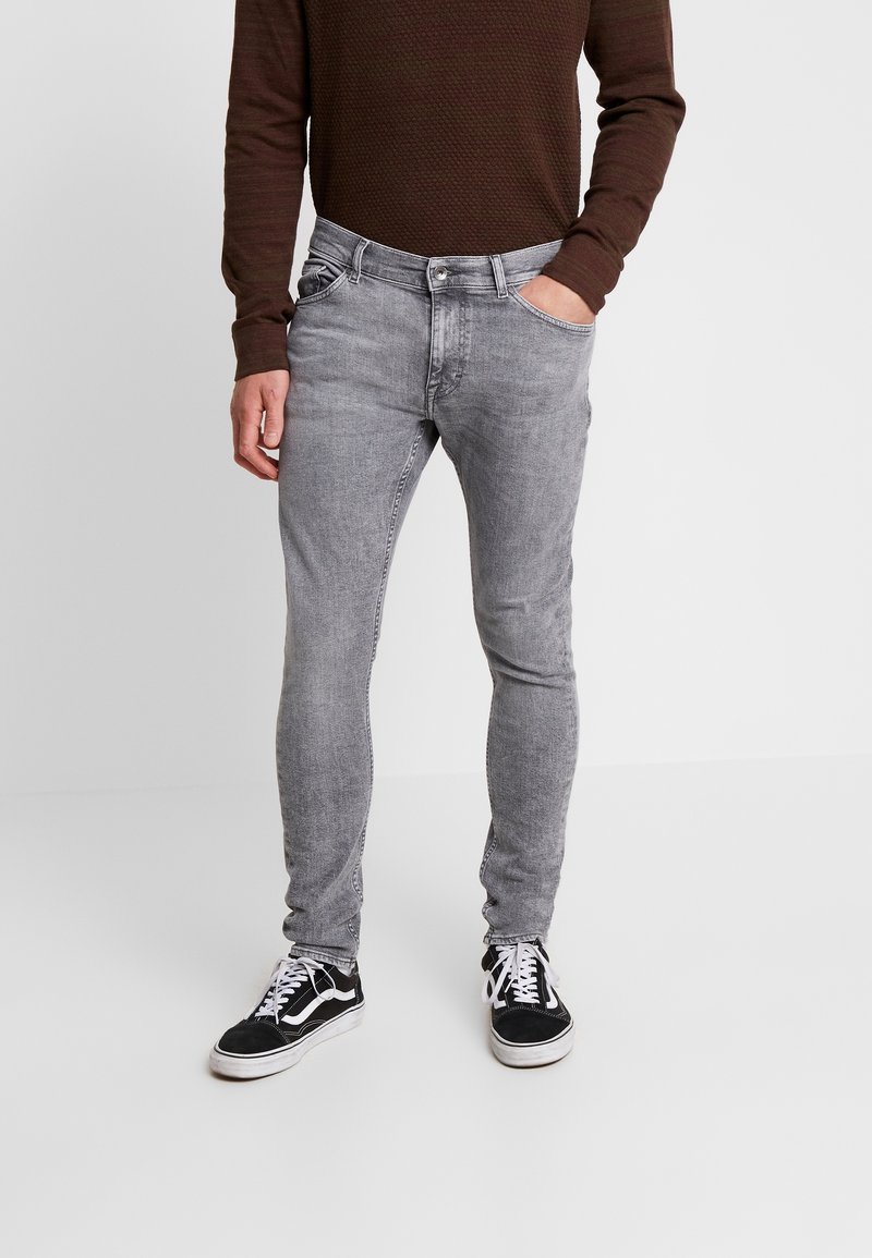 Jeans de mezclilla gris de corte ajustado con un aspecto desgastado, que cuentan con cinco bolsillos y una textura suave. Combinados con zapatillas negras y blancas.
