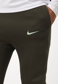 Donkergroene sweatpants met een gladde textuur en slim fit. Heeft een lichtgroene Nike-logo aan de linkerkant.