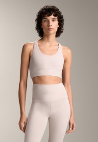 Ljusbeige sportbh med breda band och en kort design, kombinerad med höga leggings i matchande tyg och färg. Slät textur.