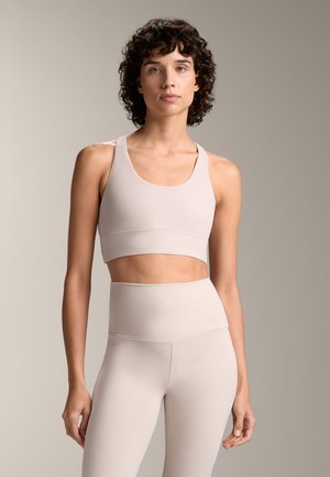 Lichtbeige sportbeha met brede banden en een cropped ontwerp, gecombineerd met high-waisted leggings van dezelfde stof en kleur. Glad textuur.