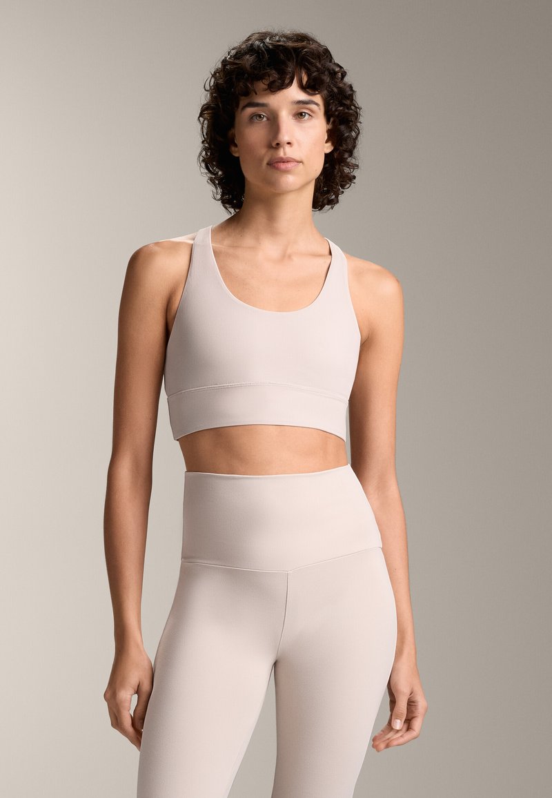 Ljusbeige sportbh med breda band och en kort design, kombinerad med höga leggings i matchande tyg och färg. Slät textur.