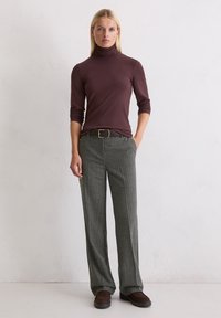 Brązowy sweter w golf połączony z szarymi spodniami w kratę, spięty ciemnobrązowym paskiem z złotą klamrą. Całość dopełniają casualowe buty.