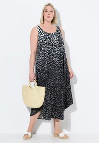 Ärmelloses Maxikleid mit Leopardenmuster in Schwarz und Grau, das ein fließendes Design mit einem seitlichen Schlitz aufweist und mit einer gewebten Strohtasche kombiniert ist.