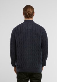 Ciemnoniebieski sweter robiony na drutach z wzorem w warkocz, z wysokim kołnierzem oraz ściągaczami na mankietach i dolnej krawędzi, wykonany z miękkiej tkaniny o fakturze.