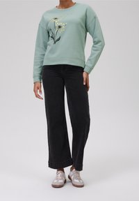 Mentolový svetr s květinovým vzorem a zlatými akcenty, v kombinaci s černými džíny s vysokým pasem a světle šedými teniskami. Ležérní střih a textura.