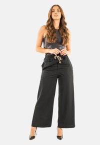 Pantalones anchos negros con cintura ajustable y herrajes plateados, combinados con una blusa metálica sin mangas. Textura de tela suave.