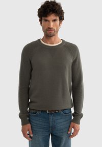Olivroheline kudum, ribakonstruktsiooniga, ümmarguse kaelusega ja ragslansleeved, kaasas siniste denimsteemadega. Lihtne disain, ilma mustriteta.