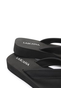 Black flip-flops with a matte textured footbed, featuring fabric straps and "LASCANA" logo on the sole. Simple and lightweight design.