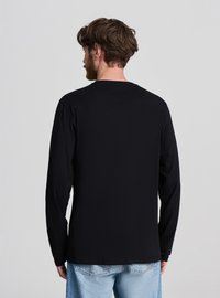 Maglietta nera a maniche lunghe, scollo rotondo, vestibilità comoda, realizzata in materiale morbido. Include un orlo dritto e un design minimalista, senza loghi visibili.