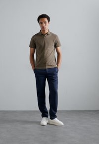 Olivovo zelená polokošeľa, tmavomodré nohavice a biele tenisky. Polokošeľa je priliehavá s golierom, zatiaľ čo nohavice sú rovné.