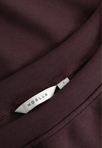 Burgundia kangas sileda tekstuuriga. Omab sildit, millel on kiri "NOELLA" ja suurus "S," koos õmmeldud äärte ja õmblusdetailidega.