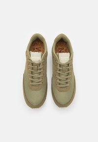 Sneaker verde oliva con materiale in rete e suede, dotati di soletta in sughero, lacci piatti e un'etichetta con logo sulla linguetta.