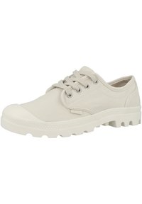 Sneaker in tela color beige chiaro con punta arrotondata, chiusura con lacci e suola in gomma con motivo di battistrada. Cuciture sottili e dettagli decorativi visibili.