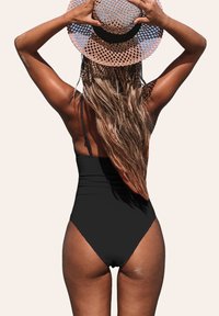 Costume da bagno intero nero con taglio alto e spalline regolabili, abbinato a un cappello di paglia rotondo e intrecciato in tonalità di rosa.