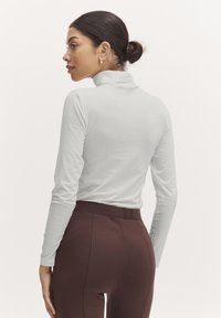 Hosszú ujjú, testhez simuló turtleneck világosszürke pamut keverékből, magas derekú, barna leggingszel párosítva. Sima textura, minimális dizájn.