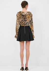Blusa a stampa leopardo con scollatura a volant, abbinata a una gonna nera plissettata con una cerniera metallica sul retro.