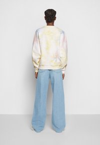 Licht pastelkleurig tie-dye sweatshirt met oversized pasvorm en verlaagde schouders, gecombineerd met wijde lichtblauwe spijkerbroek. Zachte stoftextuur.
