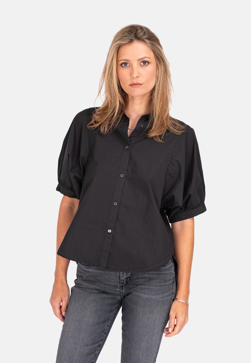 Schwarzes Hemd mit kurzen, puffigen Ärmeln. Aus glattem Stoff mit einem strukturierten Schnitt und abgerundetem Saum. Kombiniert mit dunkelgrauen Jeans.