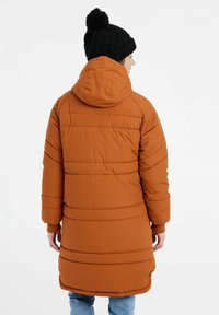 Orange pufferjakke med hætte, præget af vandrette syninger, lange ærmer, og en let indsnævret talje. Strikket sort pom-pom hue.