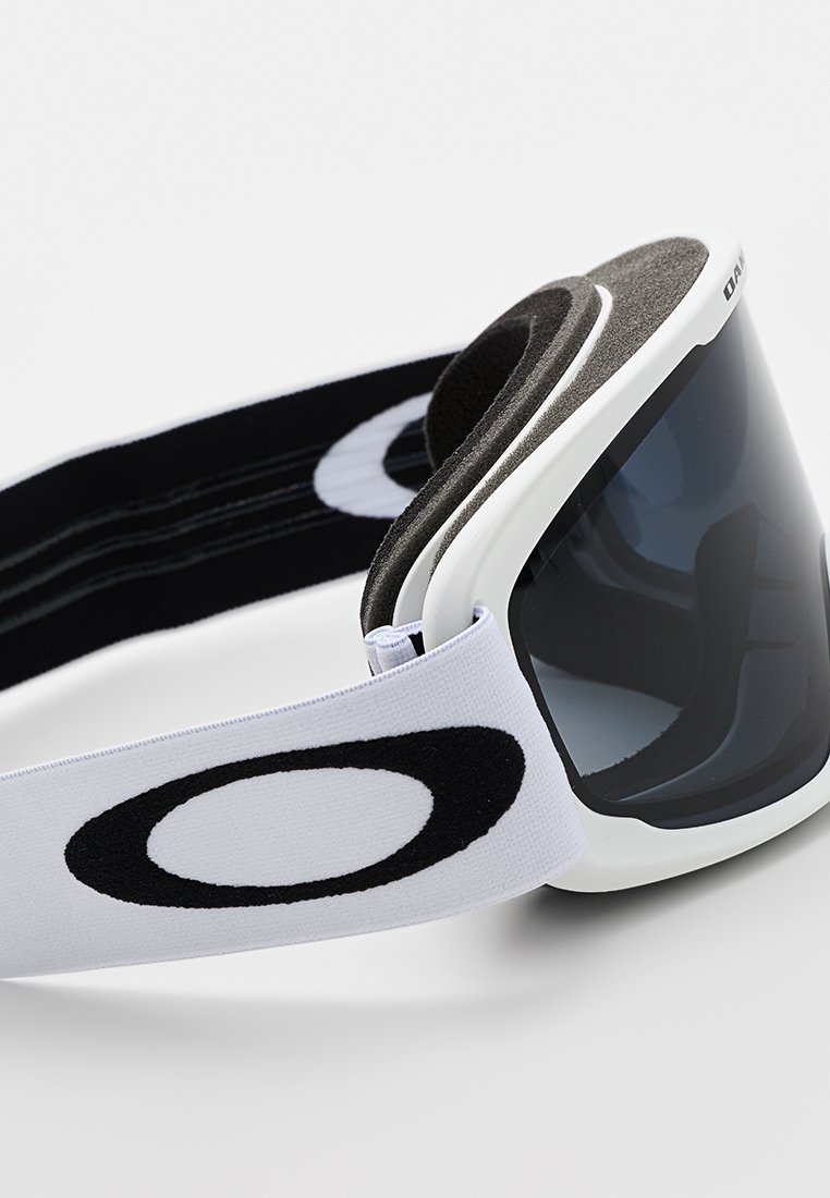Maschera da sci con lente scura curva e montatura bianca. Presenta un elastico nero con un logo ben visibile. Imbottitura in schiuma per il comfort.