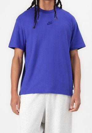 Blå Nike t-shirt lavet af bomuld, med rund hals, korte ærmer og et sort logo på brystet. Kombineret med grå sweatpants.