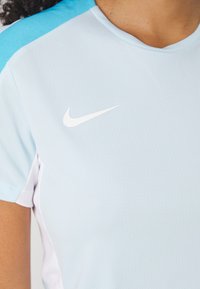 Svetlo modré športové tričko s textúrovanou tkaninou, bielym logom Nike na hrudi a kontrastnými tyrkysovými akcentmi na pleciach.