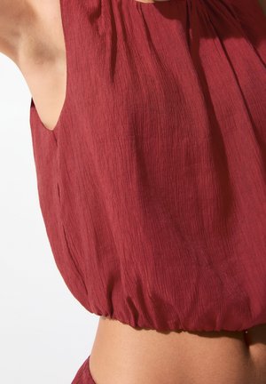 Haut texturé couleur marron foncé avec une silhouette ample en forme de ballon et des emmanchures larges. Comprend un ourlet froncé pour une coupe décontractée. Finition du tissu lisse.