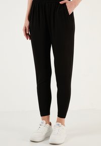 Zwarte tapered joggingbroeken met een elastische tailleband, zijzakken, een gladde textuur, gedragen met witte sneakers.