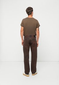 Brune denimjeans med rett ben design, kombinert med en olivengrønn, kortermet bomull t-skjorte, iført beige sneakers.