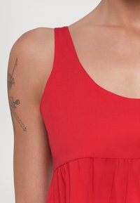 Abito rosso senza maniche con corpetto aderente e gonna svasata. Realizzato in tessuto morbido, presenta una superficie liscia e dettagli di cucitura minimi.