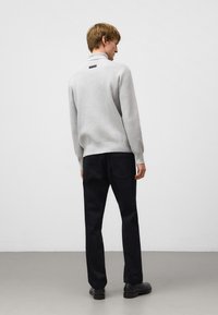 Jasnoszary sweter z dzianiny z wysokim kołnierzem, w połączeniu z ciemnymi dżinsami i czarnymi butami. Z tyłu znajduje się mała czarna metka.