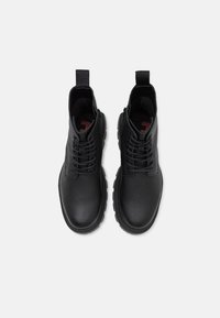 Bottes en cuir noir avec une surface texturée, design à lacets, bout rond et une poignée sur le col ; semelle en caoutchouc robuste.