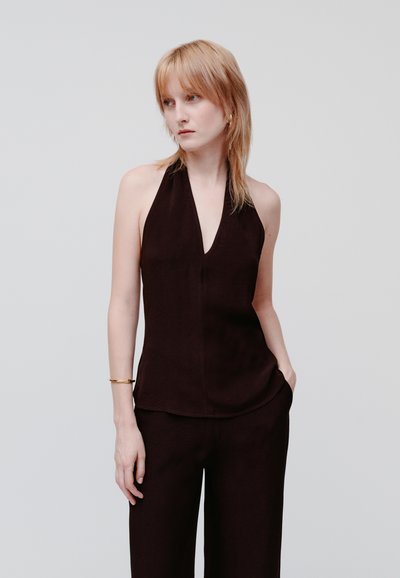 Top nero a halter con scollatura a V profonda, texture liscia e vestibilità slim. Abbinato a pantaloni a gamba larga coordinati. La modella posa con una mano in tasca.