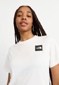 Tricou alb din bumbac, cu mâneci scurte, având un patch cu logo negru pe pieptul stâng. Textură netedă, decolteu rotund.