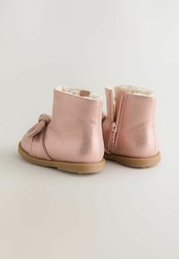 Bocanci metalici roz, cu căptușeală din blană sintetică, fermoar la spate și fundă decorativă pe lateral. Talpă din cauciuc plat.