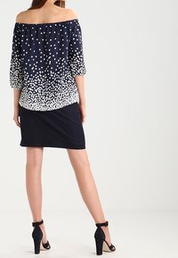 Marinblus utan axlar med vita prickar, 3/4 puffärmar och en enfärgad svart kjol, tillsammans med svarta högklackade sandaler.